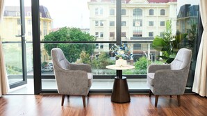 Ein Zimmer mit zwei grauen Sesseln, einem kleinen runden Tisch mit einer Vase und einem großen Fenster mit Blick auf ein Gebäude.