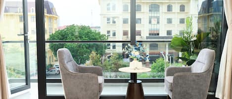 A room with two grey armchairs, a small round table with a vase, and a large window with a view of a building.