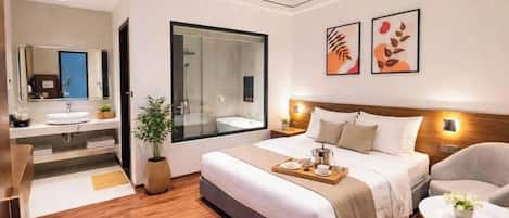 Una habitación de hotel moderna con una cama grande, una mesita de noche, una silla, una mesa redonda y un baño con espejo y lavamanos.
