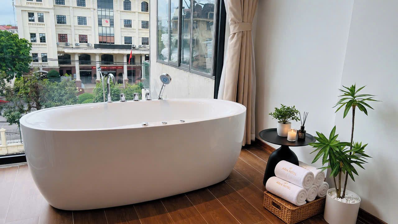Un baño moderno con una bañera independiente, una ventana con vistas a edificios y una pequeña mesa con toallas y una planta.