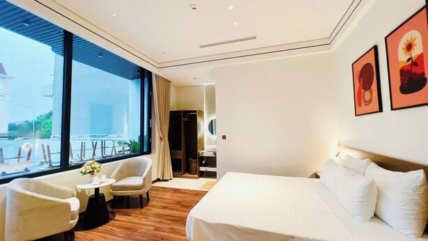 Ein Hotelzimmer mit einem Bett, einer Sitzecke mit Stühlen, einem kleinen Tisch mit einer Vase und großen Fenstern mit Blick.