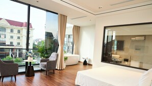 Ein modernes Hotelzimmer mit einem großen Bett, einer Couch, einem kleinen Tisch und Blick auf die Stadt durch große Fenster.