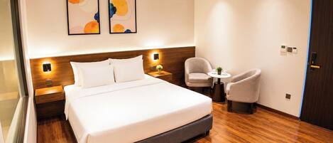 A hotel room with a large bed, a bedside table, a chair, and two abstract paintings on the wall.