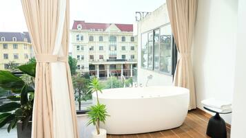 Un baño moderno con una bañera grande, una planta en maceta y vistas a un edificio con múltiples ventanas.