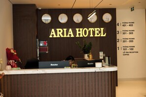En hotelfacade med reception og et skilt der siger 'ARIA HOTEL', samt rumnumre på væggen.