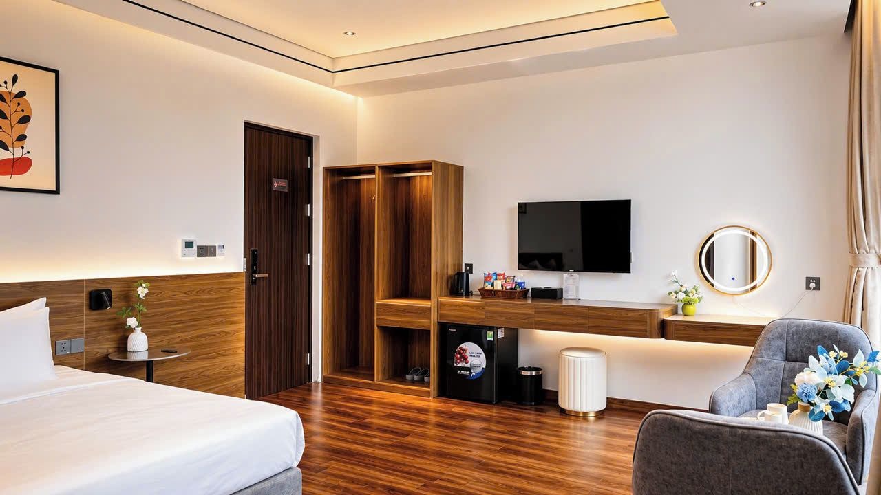 A hotel room with a bed, a desk, a television, a wardrobe, and a seating area.