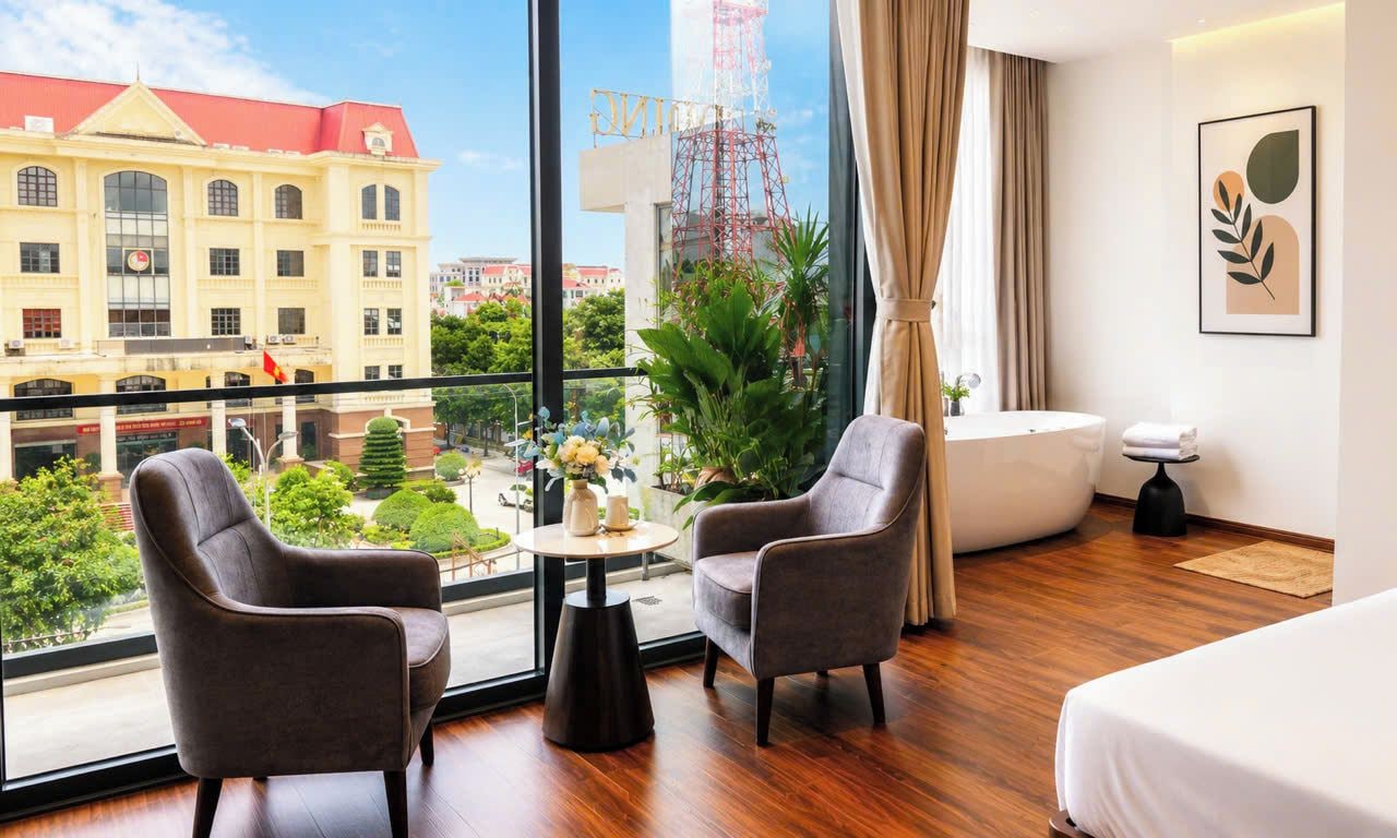 Habitació d'hotel amb un balcó, dues butaques, una taula rodona, un llit i vistes a un edifici i una zona de construcció.