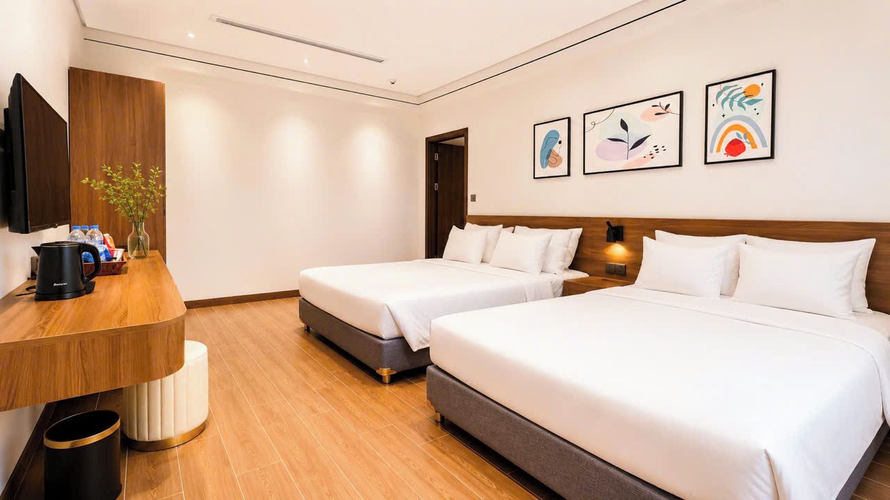 Habitación de hotel con dos camas, un escritorio de madera, un televisor y obras de arte en la pared.