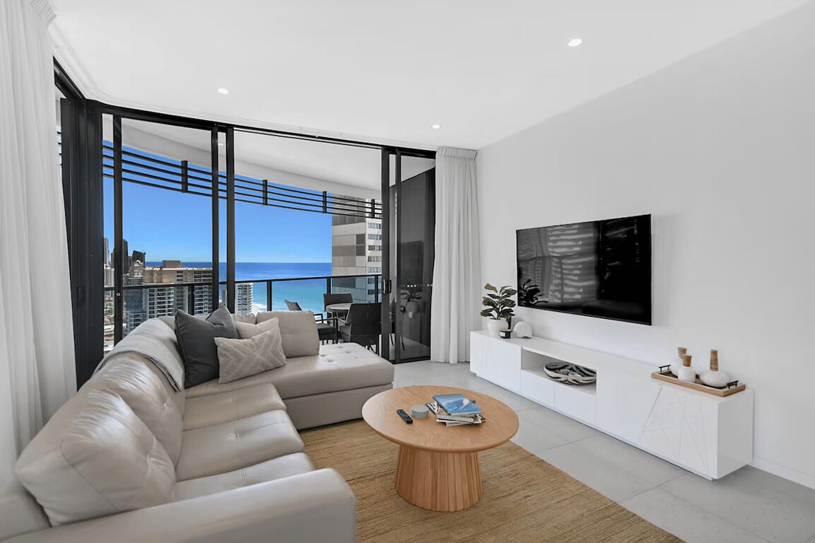 Ein modernes Wohnzimmer mit einer Couch, einem Couchtisch, einem Fernseher und einem Balkon mit Blick auf die Stadt.