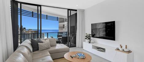 Ein modernes Wohnzimmer mit einer Couch, einem Couchtisch, einem Fernseher und einem Balkon mit Blick auf die Stadt.