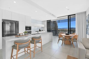 A modern kitchen with a large island, stainless steel appliances, and a dining area with a view. - Ocean and City at Oracle Level 32 (Gold Coast City)