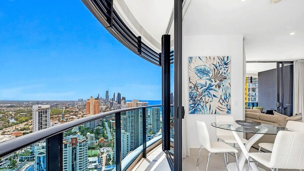A balcony with a city view, a dining area with a glass table, and a modern art piece. - Ocean and City at Oracle Level 32 (Gold Coast City)