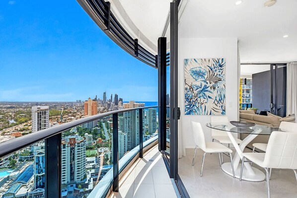 A balcony with a city view, a dining area with a glass table, and a modern art piece. - Ocean and City at Oracle Level 32 (Gold Coast City)
