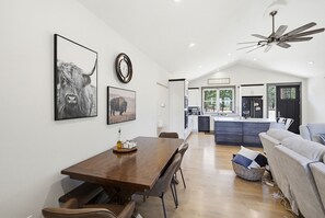 A modern kitchen with white cabinets, a dining area with a wooden table, and a ceiling fan.