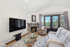 A living room with a flat-screen TV, stone fireplace, sofa, and a large window.