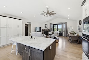A modern kitchen with a marble island, white cabinets, and a dining area with a fireplace.