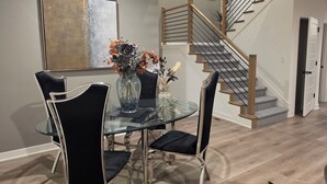 A dining area with a glass table, black chairs, and a vase with flowers. A staircase with wooden steps and metal railings is visible. - Lenexa Executive Getaway (Lenexa)