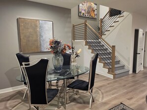 Ein Essbereich mit einem Glastisch, schwarzen Stühlen und einer Vase mit Blumen. Eine Treppe mit Holzstufen und Metallgeländern ist sichtbar.