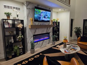 Ein modernes Wohnzimmer mit Kamin, einem flachbildfernseher darüber und einem Bücherregal mit Büchern und Dekoration.