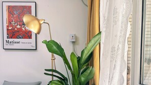 Ett rum med en brun lädersoffa, en grön växt, ett inramat konstverk på väggen och ett fönster med gardiner.