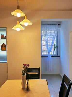 A dining area with a table, chairs, a vase with flowers, and pendant lights.