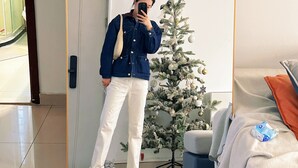 En person som tar en selfie framför en spegel i ett rum med en julgran, en säng och en stol.