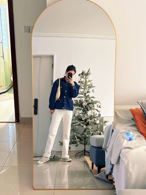 Une personne prend un autoportrait devant un miroir dans une pièce où se trouvent un sapin de Noël, un lit et une chaise.