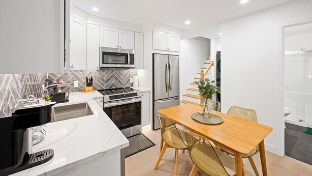 Una cocina moderna con armarios blancos, microondas, refrigerador, horno y un comedor con mesa y sillas de madera.