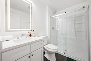 Ein modernes Badezimmer mit einem weißen Waschtisch, einem großen Spiegel, einer Toilette und einer Duschkabine.