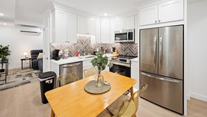 Una cocina moderna con armarios blancos, electrodomésticos de acero inoxidable y un comedor con mesa y sillas de madera.