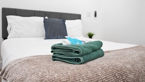 Una cama bien hecha con un cabecero gris, almohadas blancas y a rayas, y una toalla verde sobre la cama.