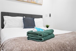 Ein ordentlich bezogenes Bett mit grauem Kopfteil, weißen und gestreiften Kissen sowie einem grünen Handtuch.