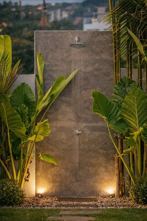Eine Dusche aus Beton mit Wasserspiel, umgeben von tropischen Pflanzen.