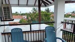 A covered balcony with two blue plastic chairs and a small table, overlooking a residential area with red-tiled roofs and greenery. - The Kumatha Residence,Second Floor Studio apartment, 5 minutes walk to the beach (Negombo)
