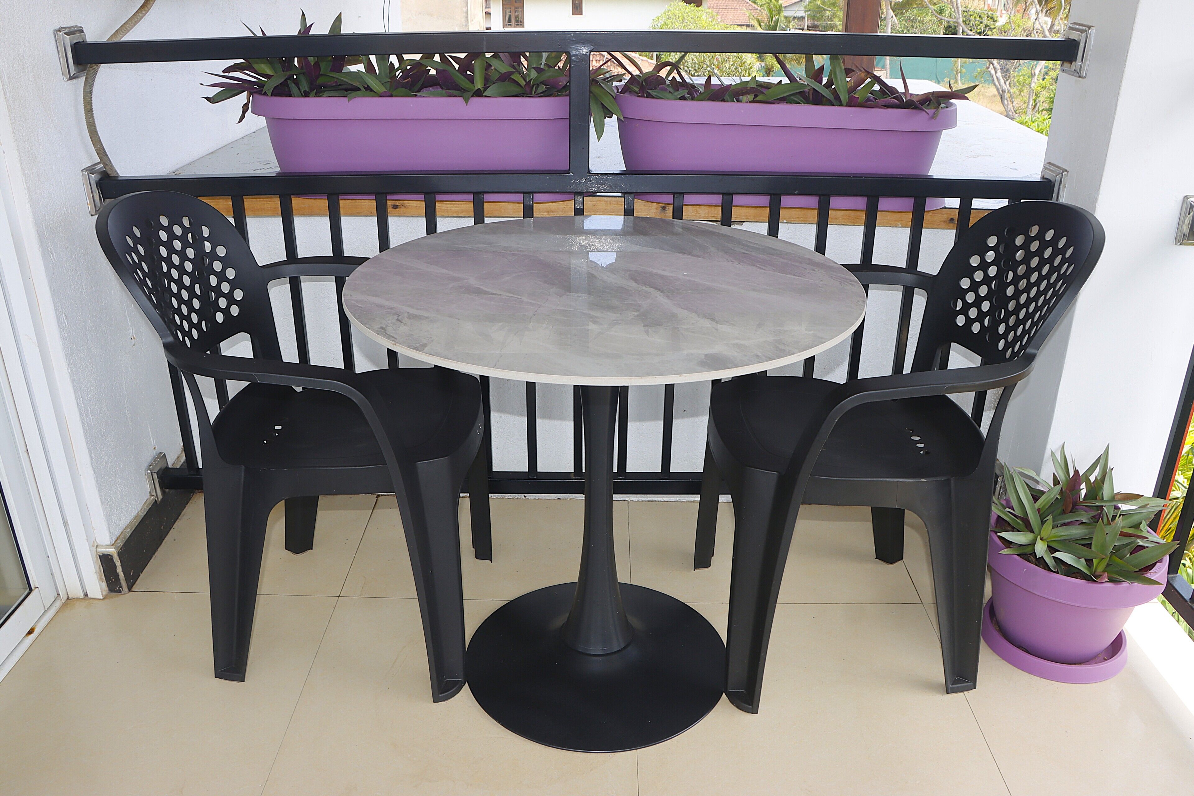 A small outdoor seating area with a round table and two chairs, surrounded by a black metal railing.