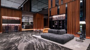 Un vestíbulo moderno con piso de mármol, un sofá seccional gris, paneles de madera, una zona de bar y una estantería.