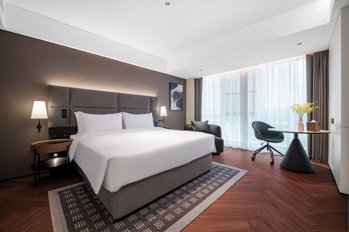 Una habitación de hotel moderna con una cama grande, un escritorio, una silla y vistas a la ciudad.