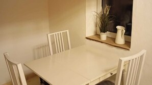 A dining area with a white table and four chairs, a window with a plant, and a wall-mounted item. - Vacation home in the green (Geestland)