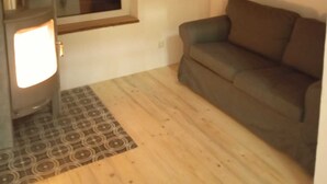 A room with a sofa, a window, a wall-mounted picture, and a stove. - Vacation home in the green (Geestland)