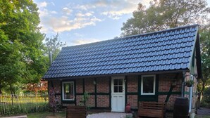 A small brick building with a tiled roof, a front door, and a window. There is a wooden table and chairs in the foreground. - Vacation home in the green (Geestland)