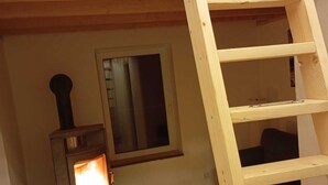 A wooden loft bedroom with a wooden ladder, a wood-burning stove, and a window. - Vacation home in the green (Geestland)
