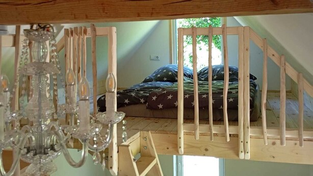 A loft bedroom with a sloped ceiling, wooden beams, a bed with star-patterned bedding, and a hanging crystal chandelier. - Vacation home in the green (Geestland)