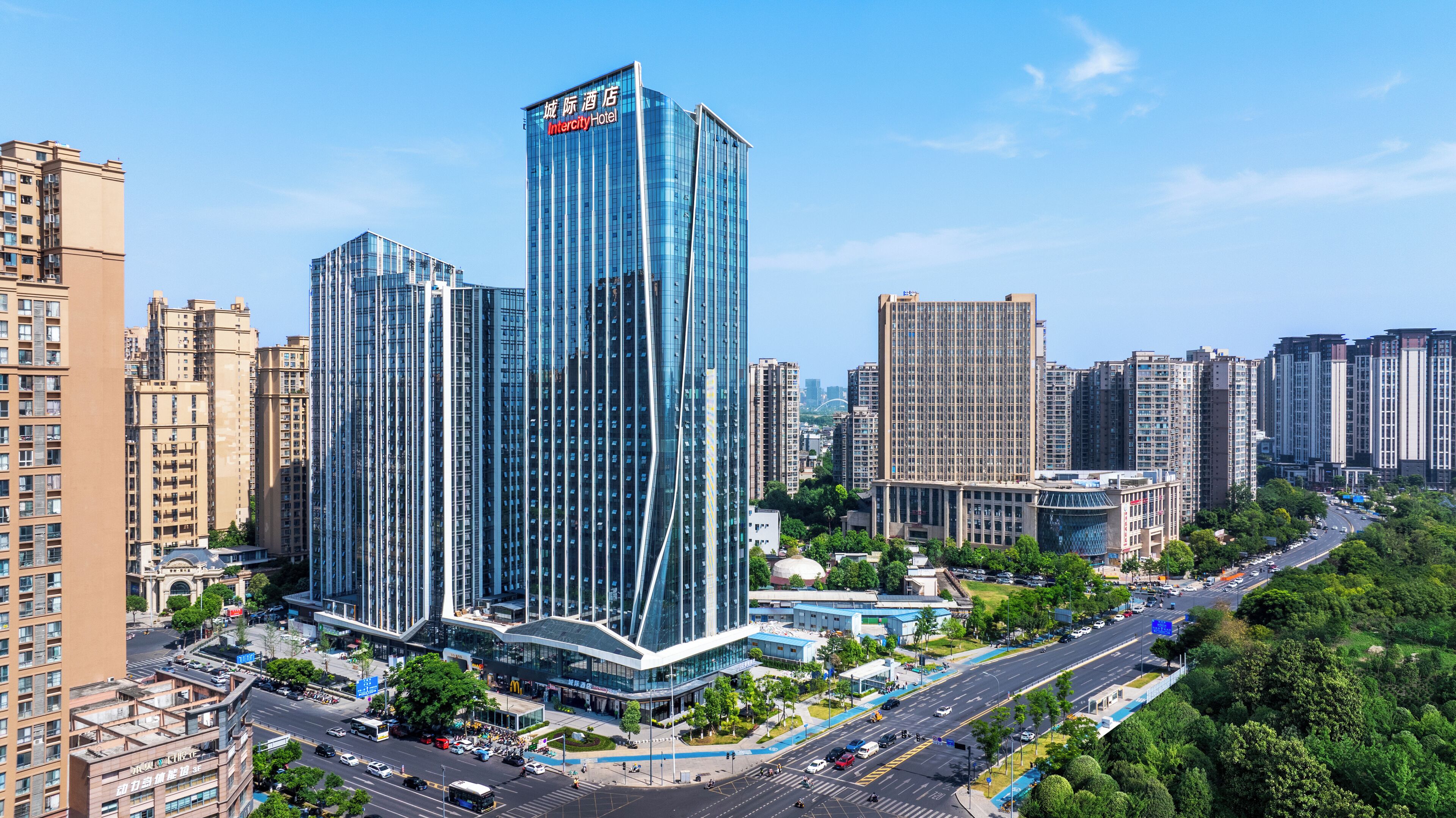 A modern hotel with a prominent glass facade, surrounded by high-rise buildings and a busy urban street.