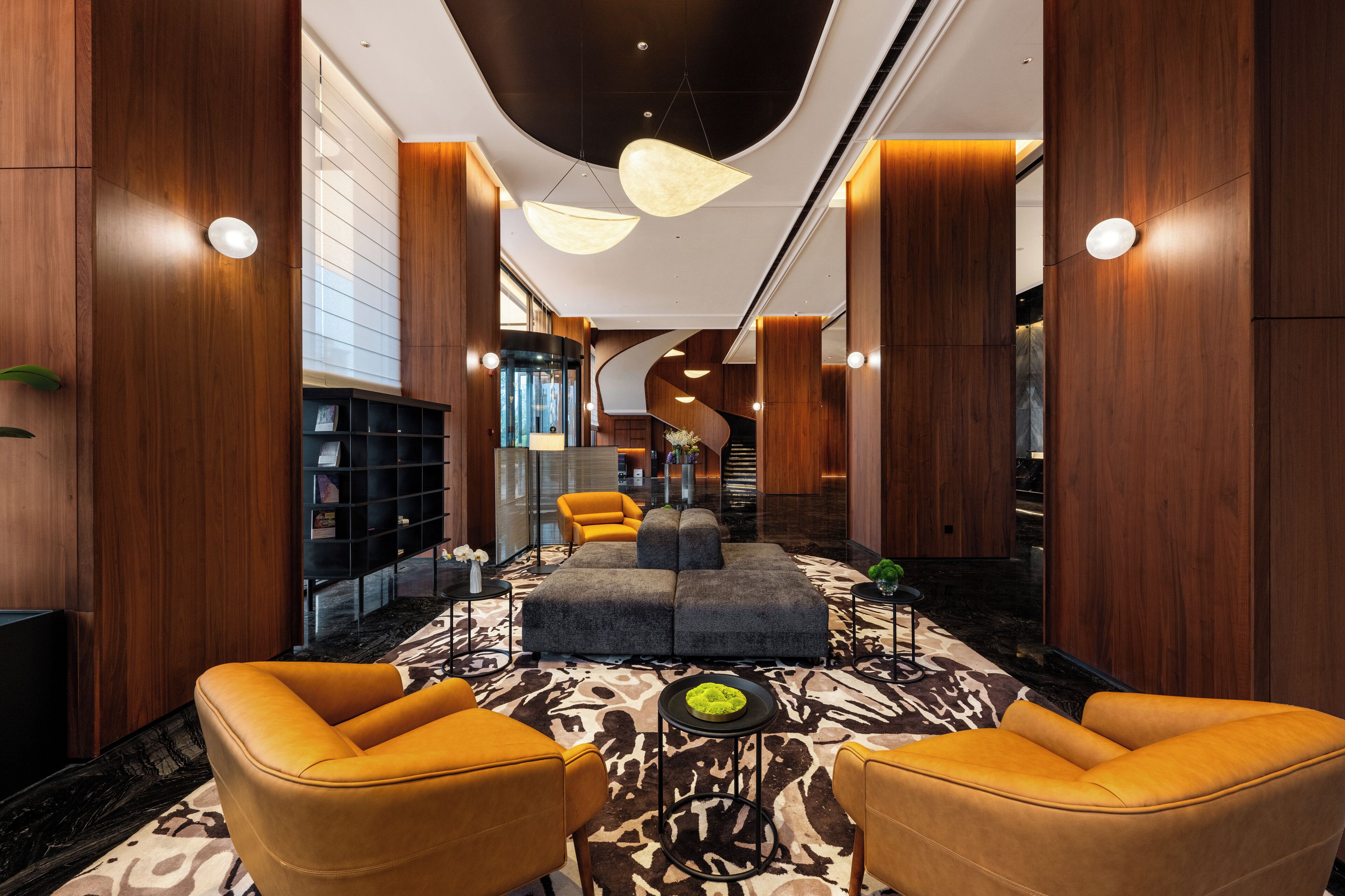 A modern lobby with a central seating area, a staircase, and wooden paneling.