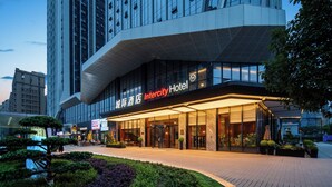 Un hotel moderno con fachada de vidrio, entrada destacada y zona exterior ajardinada.