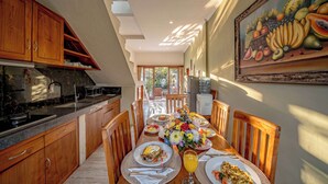A dining area with a table set for two, wooden cabinets, a kitchen area, and a fruit painting on the wall. - Villa Ciconia Ubud (Ubud)