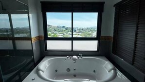 Um banheiro com uma banheira grande, uma janela com persianas e vista para a cidade.
