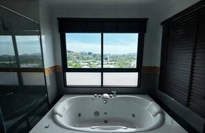 A bathroom with a large bathtub, a window with blinds, and a view of a cityscape. - Chalong Miracle Lakeview 4021 (Chalong)