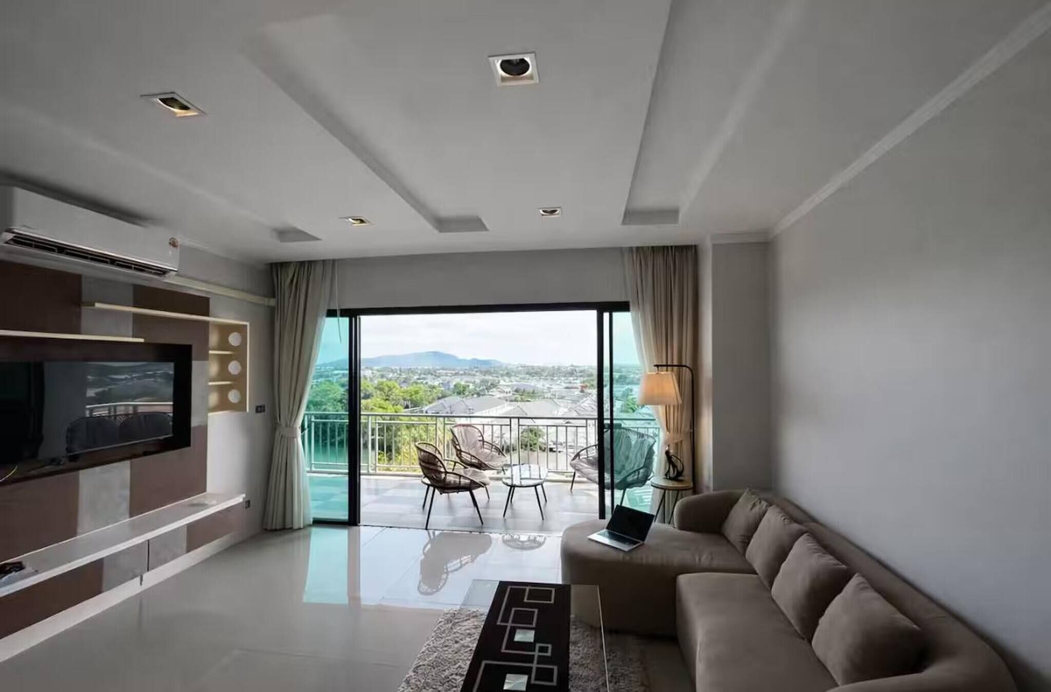 A modern living room with a flat-screen TV, a sofa, a coffee table, and a balcony with outdoor furniture.