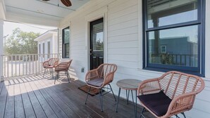 Eine überdachte Veranda mit Korbmöbeln, einem Deckenventilator und großen Fenstern.